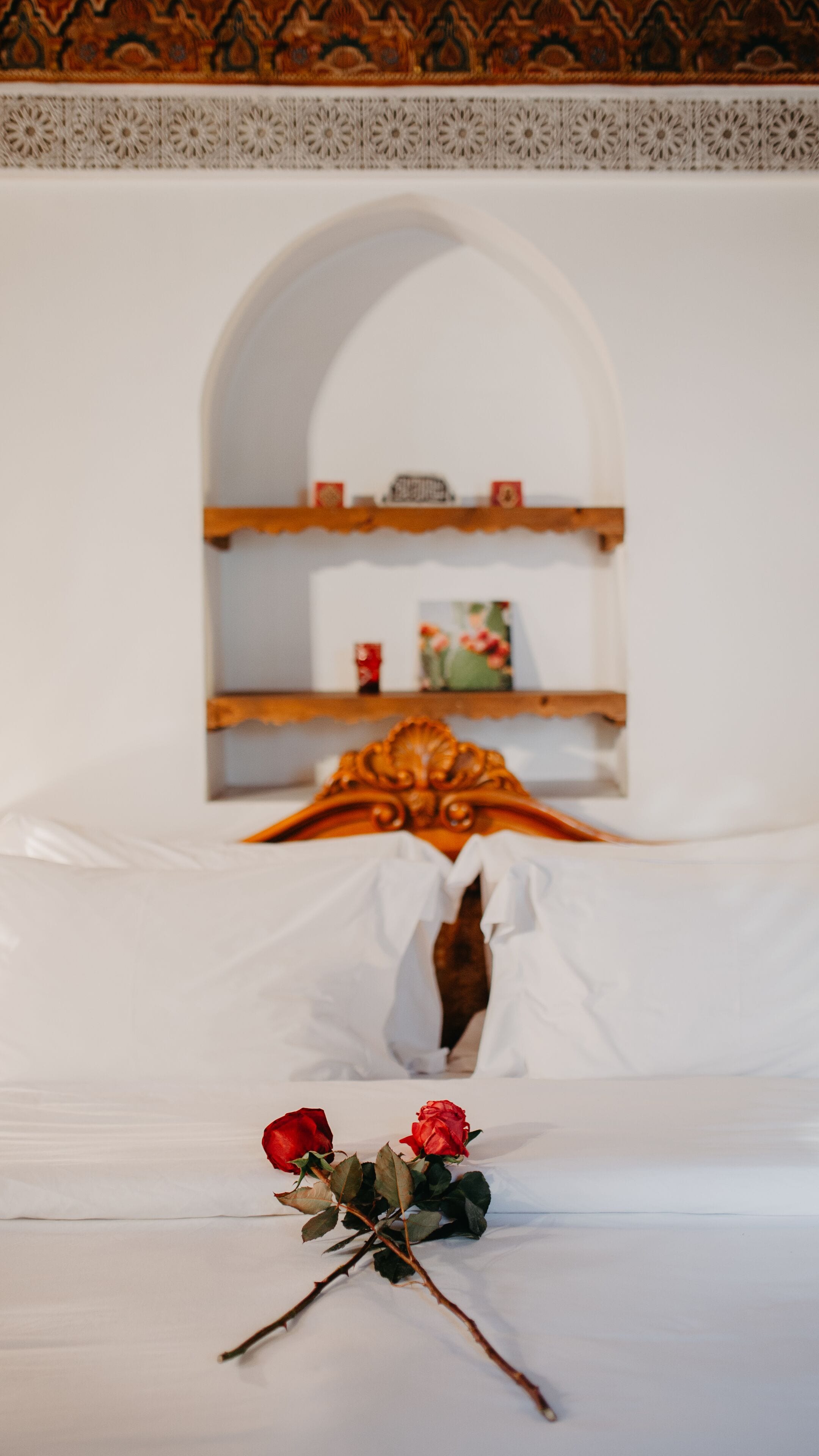 A bed with white linens, a wooden headboard, and a decorative arch above it.