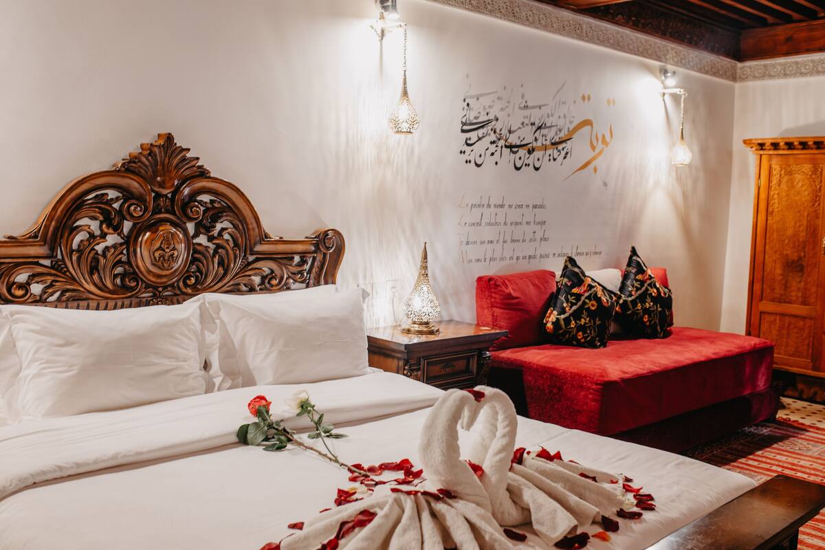 Habitación de hotel con una cama grande, un sofá rojo, un armario de madera y una pared con caligrafía árabe.