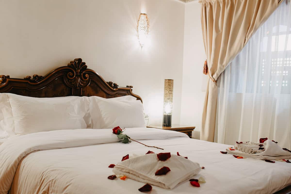 Una cama bien hecha con sábanas blancas, un cabecero de madera decorativo y una mesita de noche con un florero.