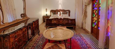 A traditional room with a bed, a wooden cabinet, a small table, and a patterned rug.