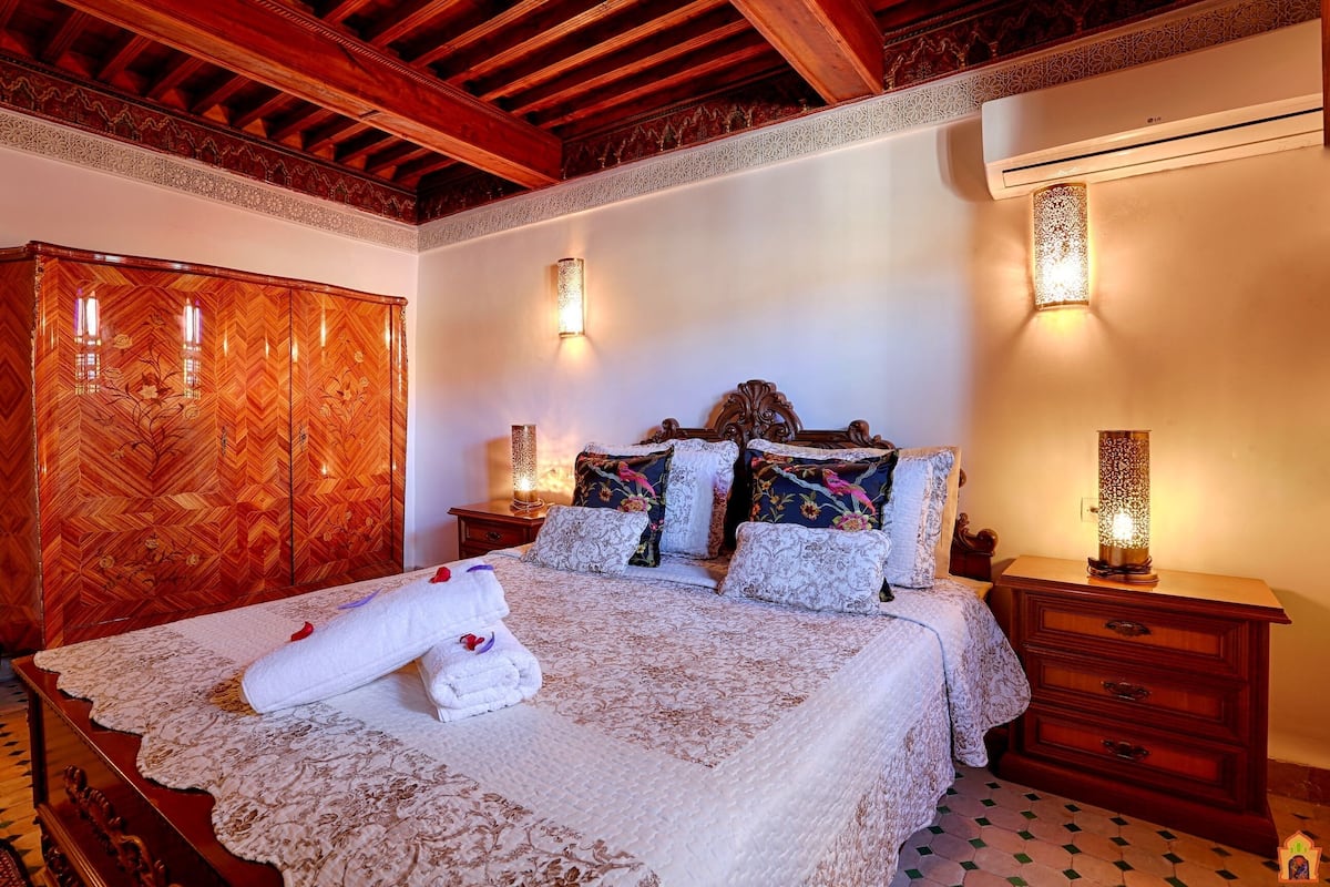 Un dormitorio con cabecera de madera, ropa de cama con estampado floral y dos lámparas de noche.