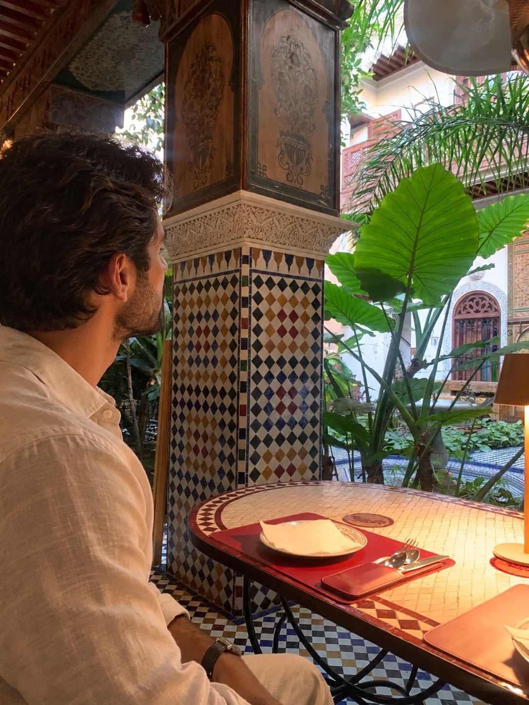 A man seated at a table with a patterned tile floor and a red table runner.