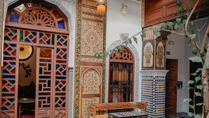 An ornate courtyard with a wooden bench and table, intricate tile patterns, and a decorative archway. - Riad TOYOUR (Fes)