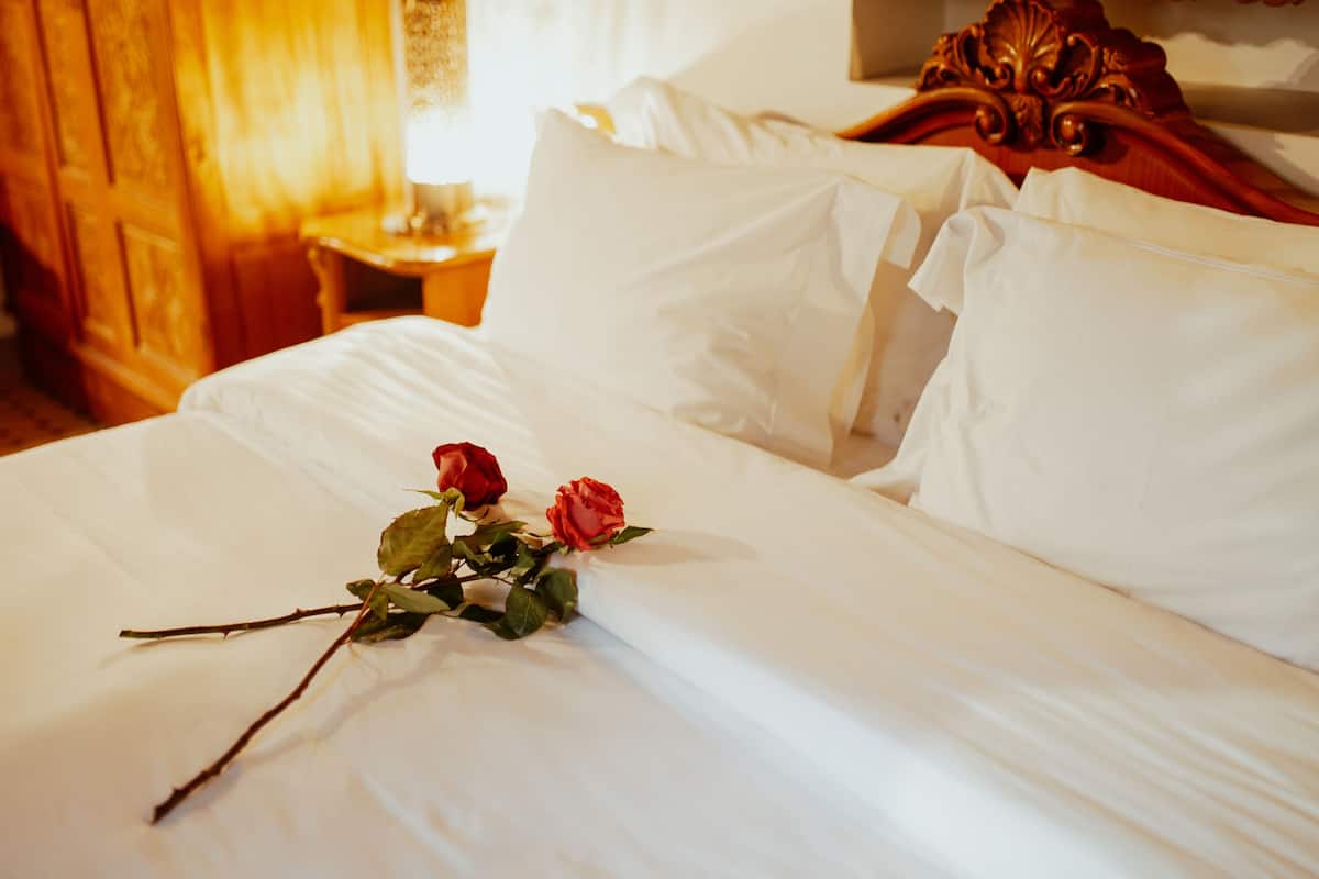 Una cama con sábanas blancas y dos rosas rojas.