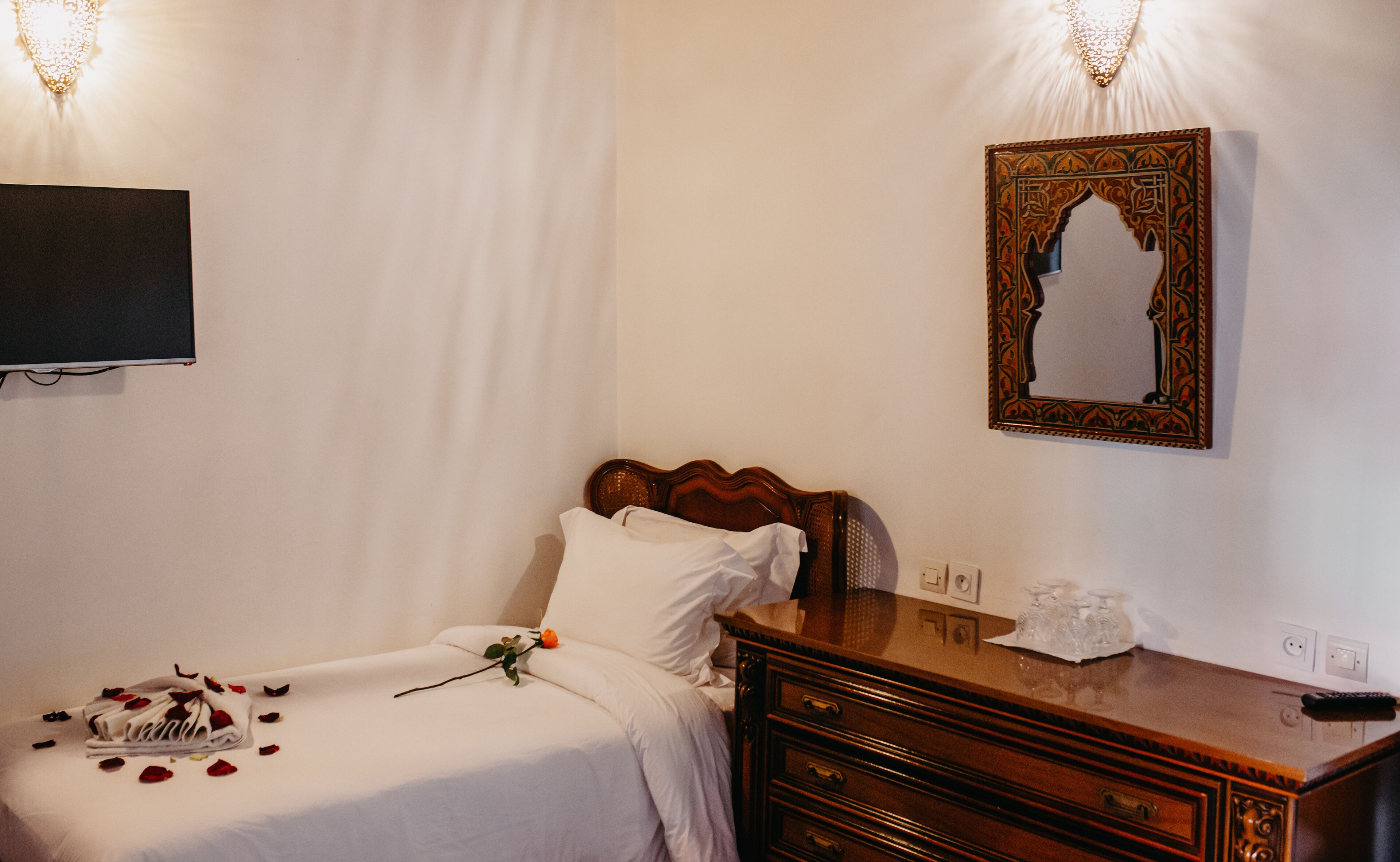 A hotel room with a bed, a wooden dresser, a mirror, and a wall-mounted TV.