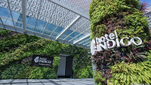 Exterior del Hotel Indigo Singapore Katong, con fachada de vidrio moderna, exuberantes jardines verticales y un letrero llamativo.
