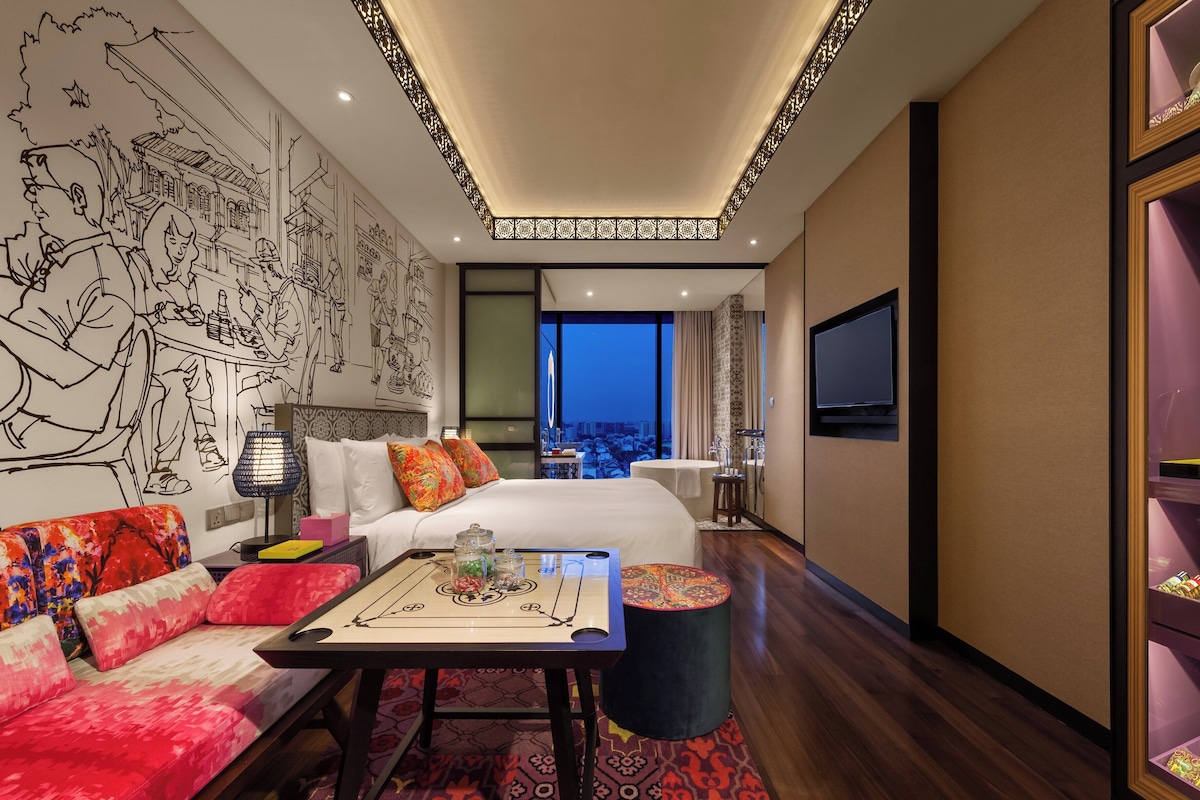A hotel room with a bed, a sofa, a coffee table, and a wall with a mural.