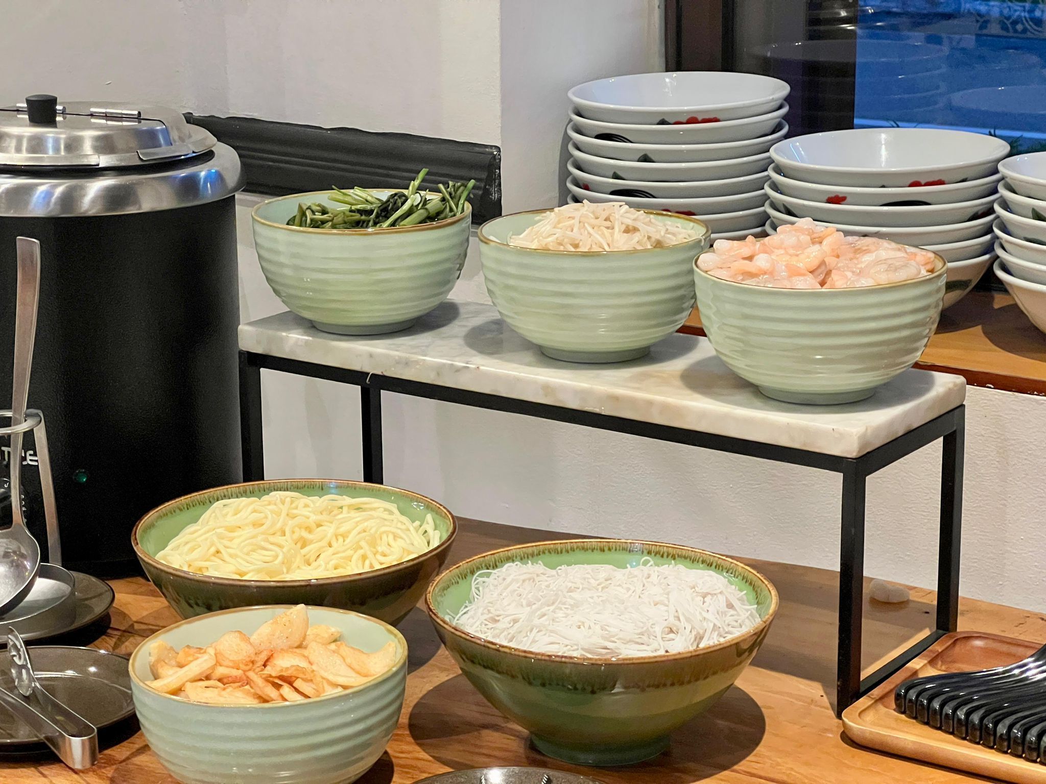 Una mesa de bufé con diversos alimentos, incluyendo tazones de fideos, arroz y mariscos.