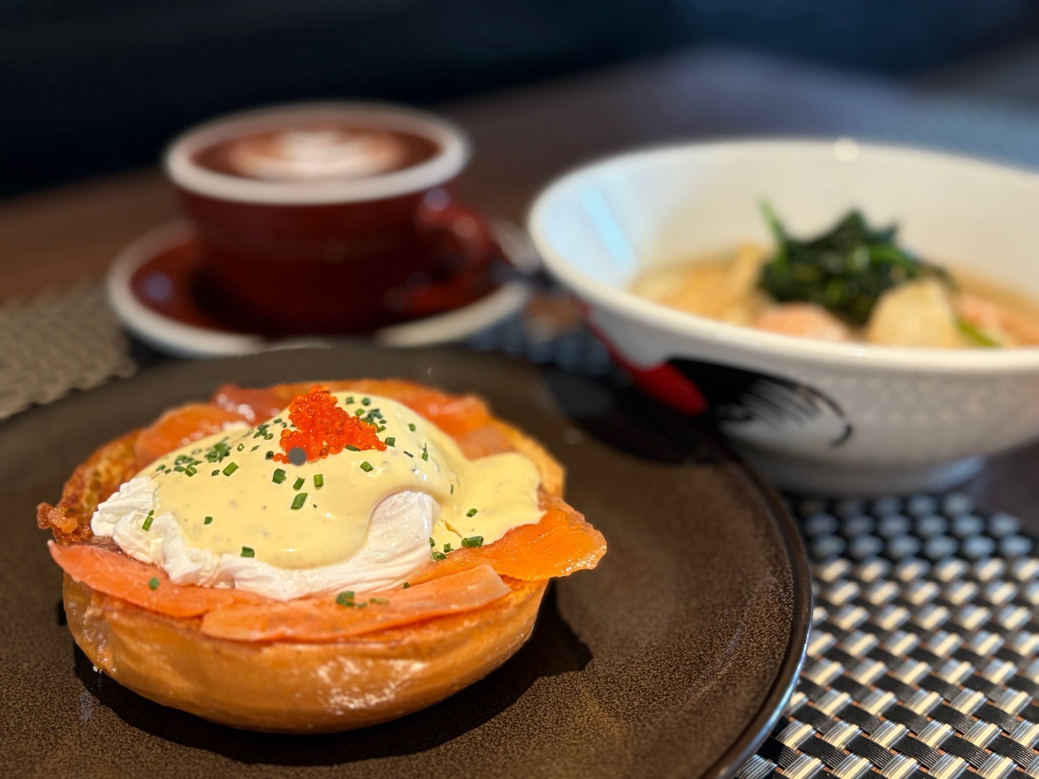 A breakfast setting with a poached egg on toast, salmon, and a bowl of soup.