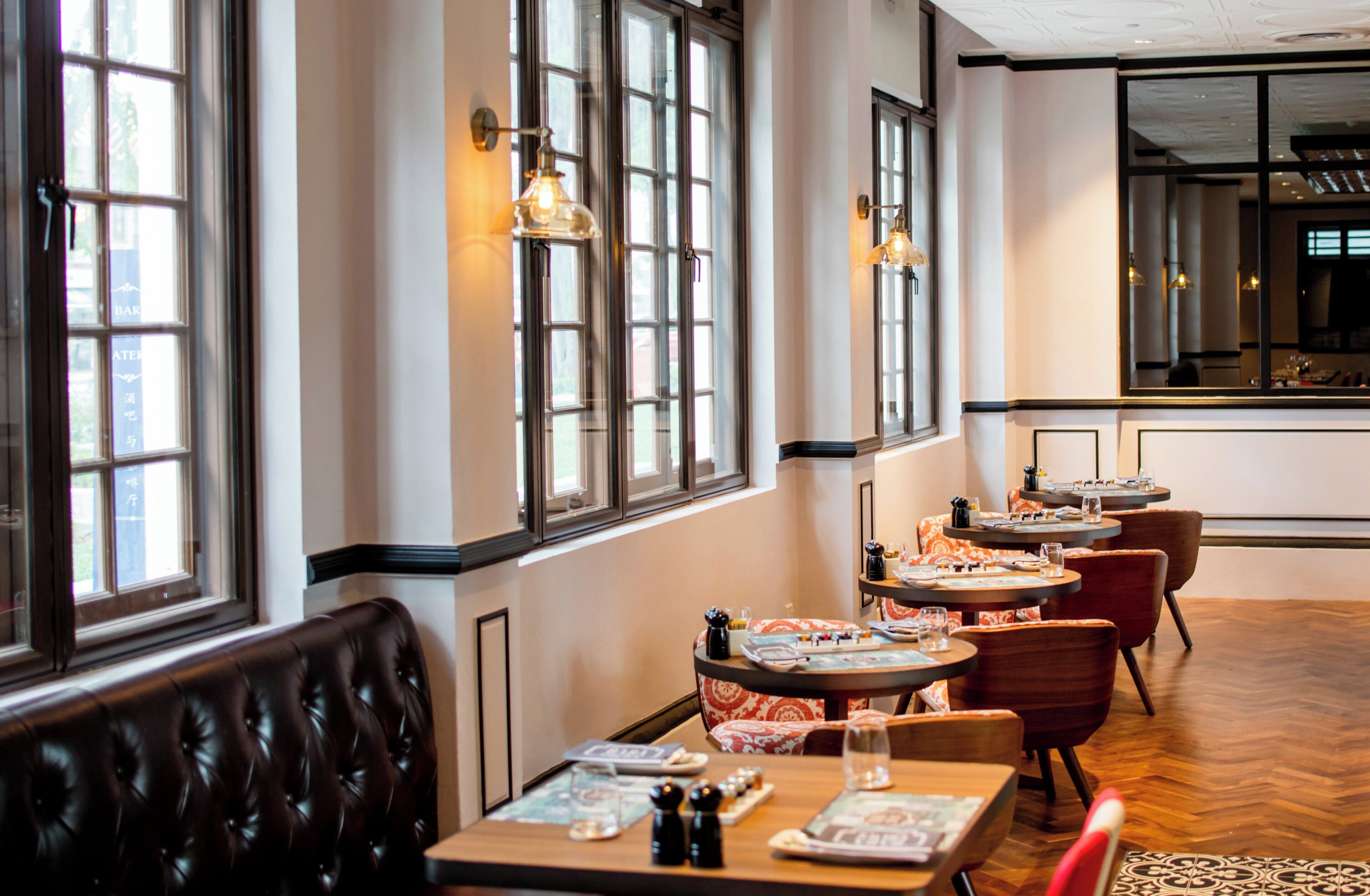 A restaurant interior with multiple tables and booths, large windows, and a high ceiling.