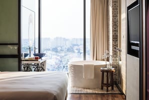 A hotel room with a large window, a bathtub, a bed, a vanity with a mirror, and a television. - Hotel Indigo Singapore Katong  by IHG (Singapore)