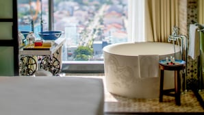 Habitación de hotel moderna con una bañera grande, vistas a la ciudad y una mesita con un cuenco y una botella.