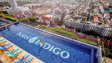 A rooftop pool with 'hotel INDIGO' written on the water, surrounded by lounge chairs and a cityscape view.