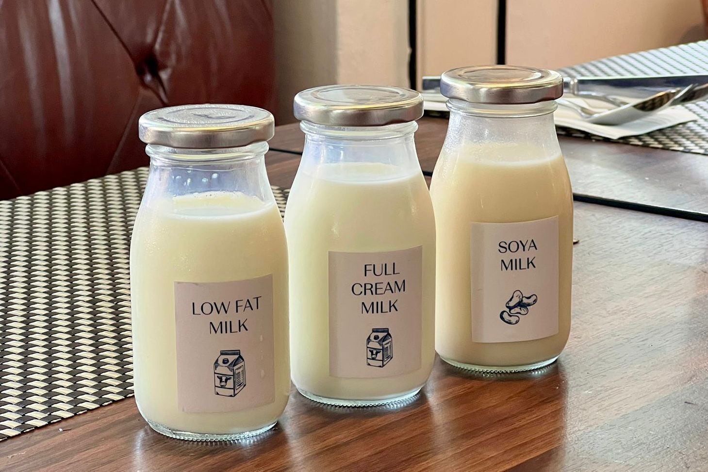 Tres botellas de vidrio con leche y etiquetas sobre una mesa de madera.