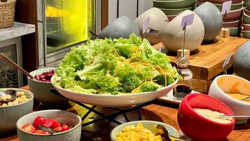 Une table de buffet proposant divers plats, notamment un grand saladier rempli de salade, des bols de maïs et un bol rouge de sauce.