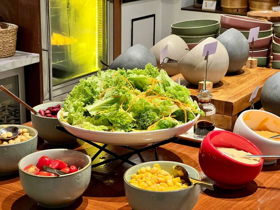 Une table de buffet proposant divers plats, notamment un grand saladier rempli de salade, des bols de maïs et un bol rouge de sauce.