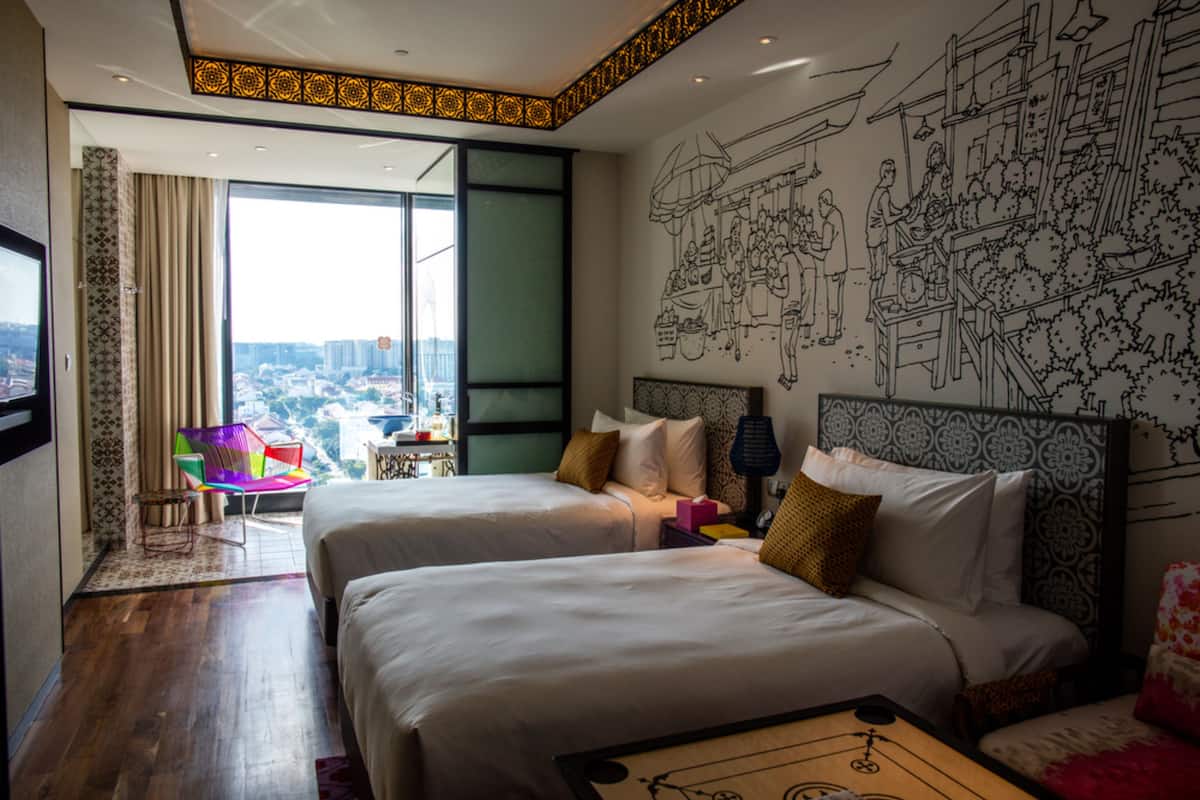 A hotel room with two beds, a large window, and a city view.