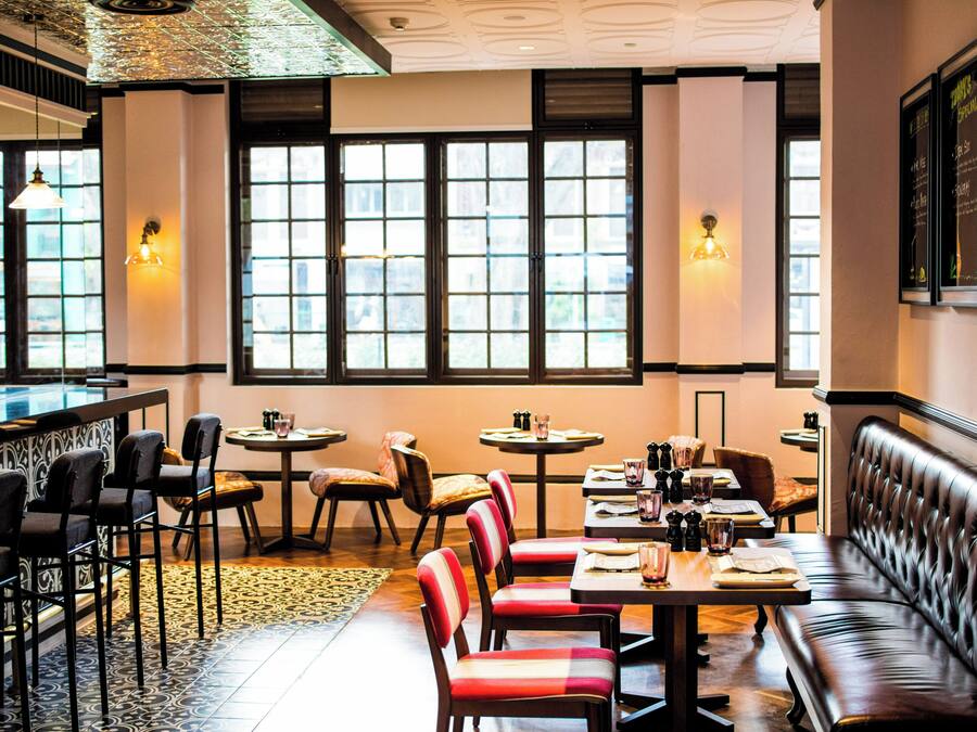 Un interior de restaurante con barra, disposición de mesas y grandes ventanales.