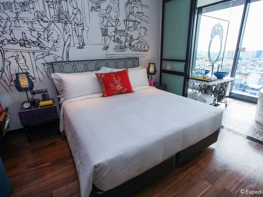 A modern hotel room with a large bed, a city view, a dining area with a black and white mural, and a small kitchen area.