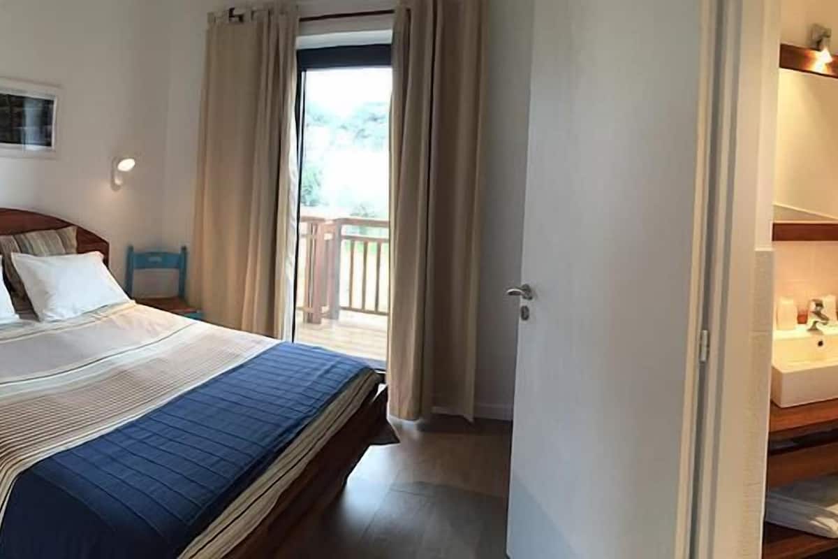 Une chambre d’hôtel avec un lit, une salle de bain équipée d’un lavabo et d’un miroir, et une vue sur l’extérieur.