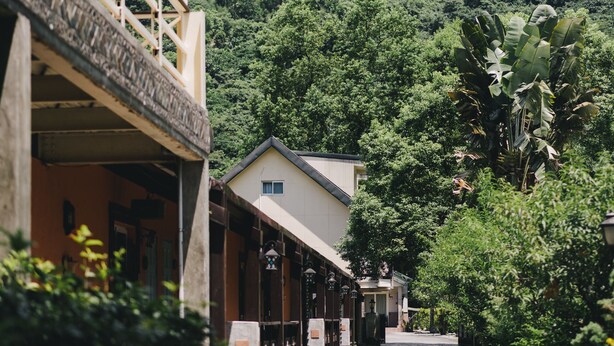 A pathway leading to a building with a balcony, surrounded by lush greenery and a hilly backdrop. - Monet Garden B&B (Shoufeng)
