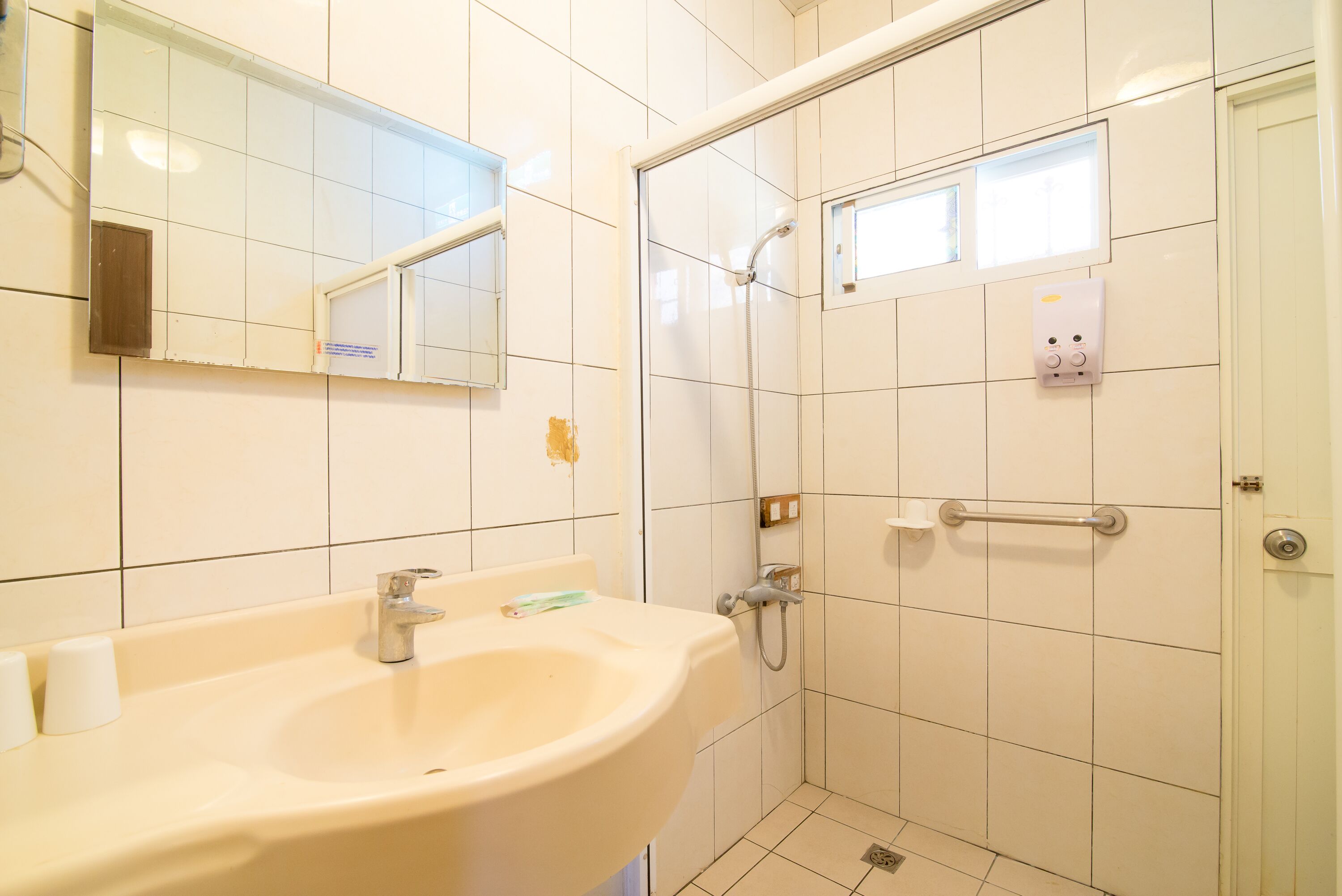 A bathroom with a sink, mirror, shower, and hand dryer.