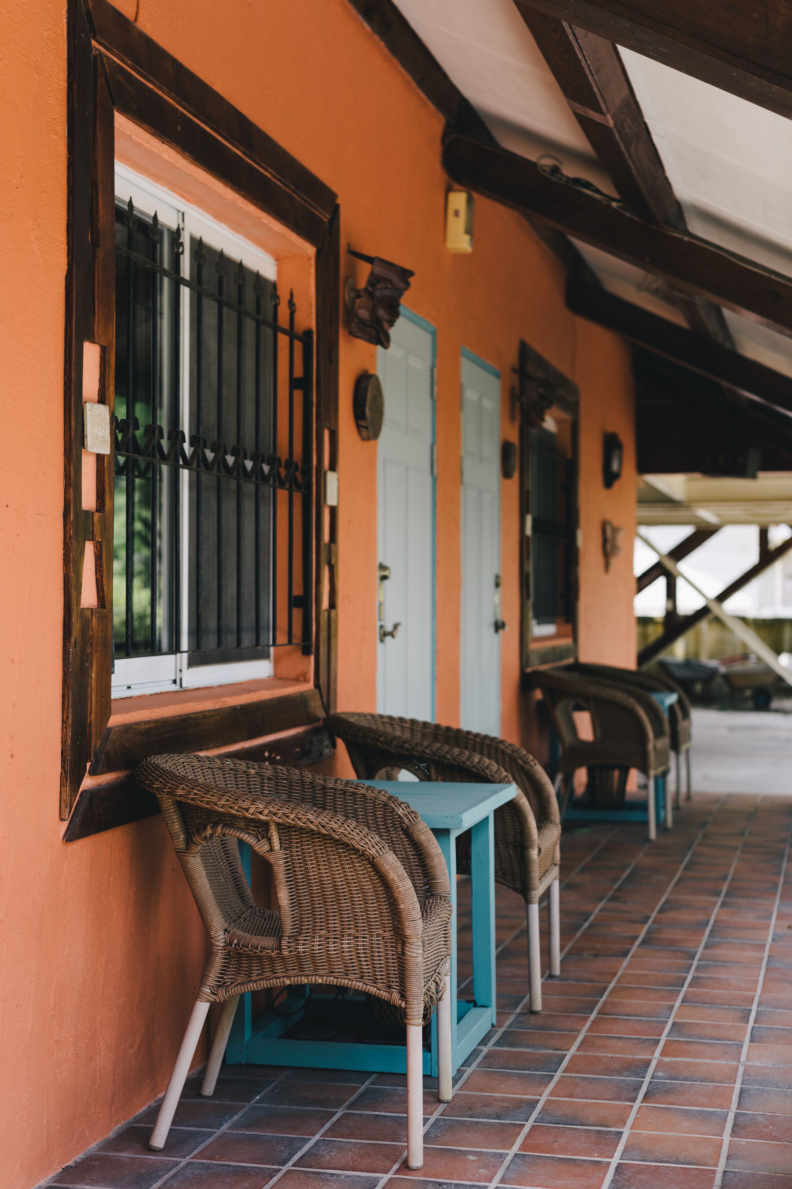 A row of wicker chairs and tables on a tiled patio with orange walls and a white door.