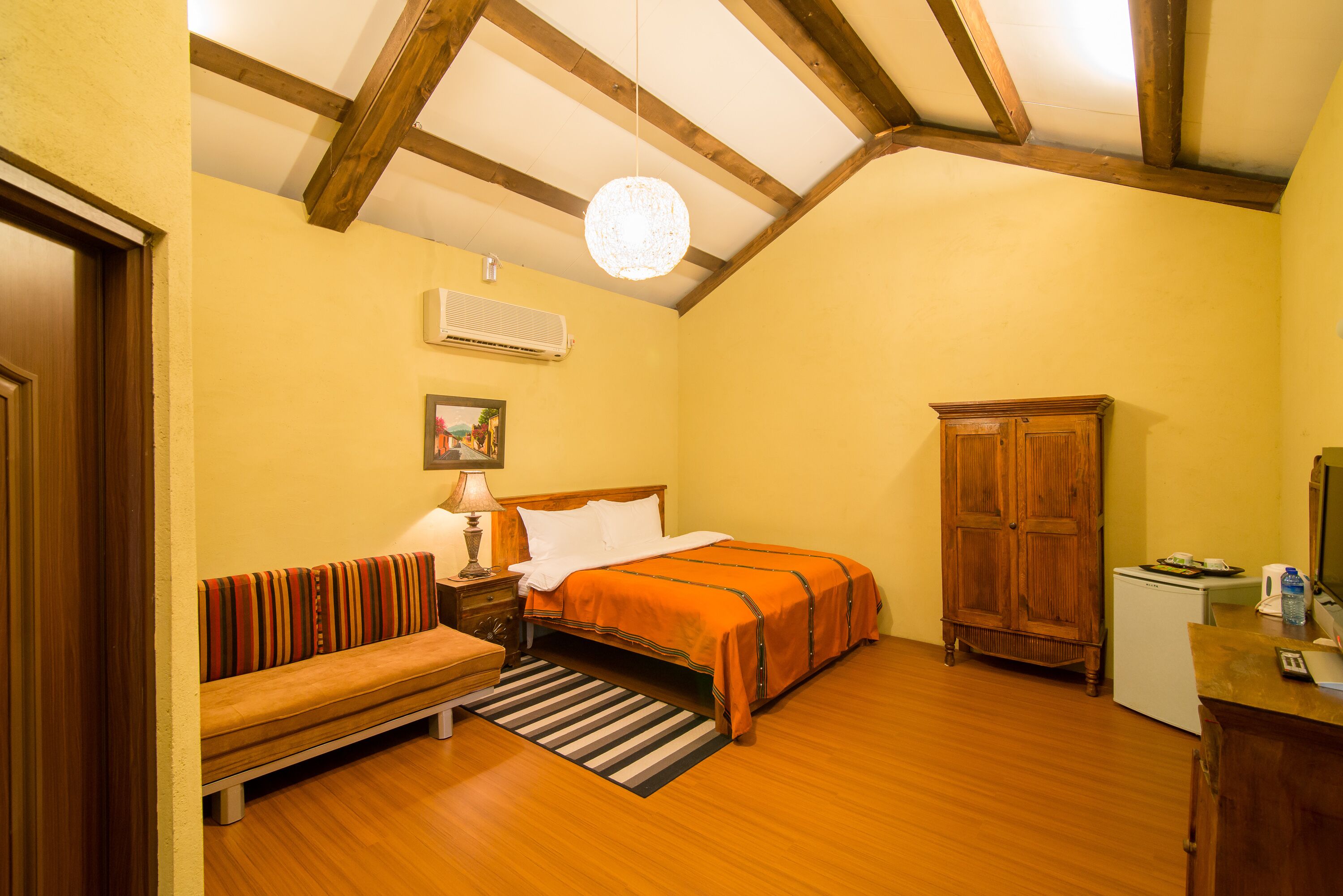 A bedroom with a bed, a wooden bench, a desk, and a wardrobe.