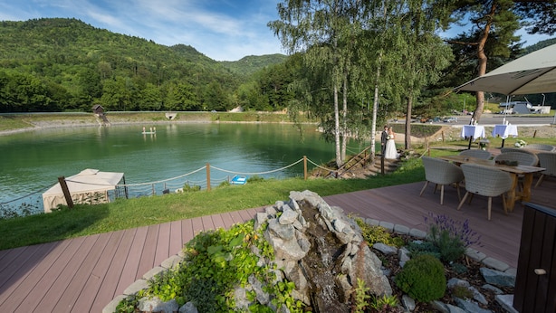 A lakeside deck with outdoor seating, a small waterfall feature, and a view of the lake and surrounding hills.