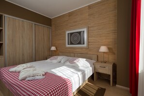 Une chambre d’hôtel avec un grand lit, deux tables de chevet, une tête de lit en bois, une œuvre d’art encadrée au mur et un rideau rouge.