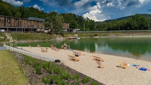 A lakeside resort with a pebble beach, lounge chairs, and a wooden building with a sloped roof.