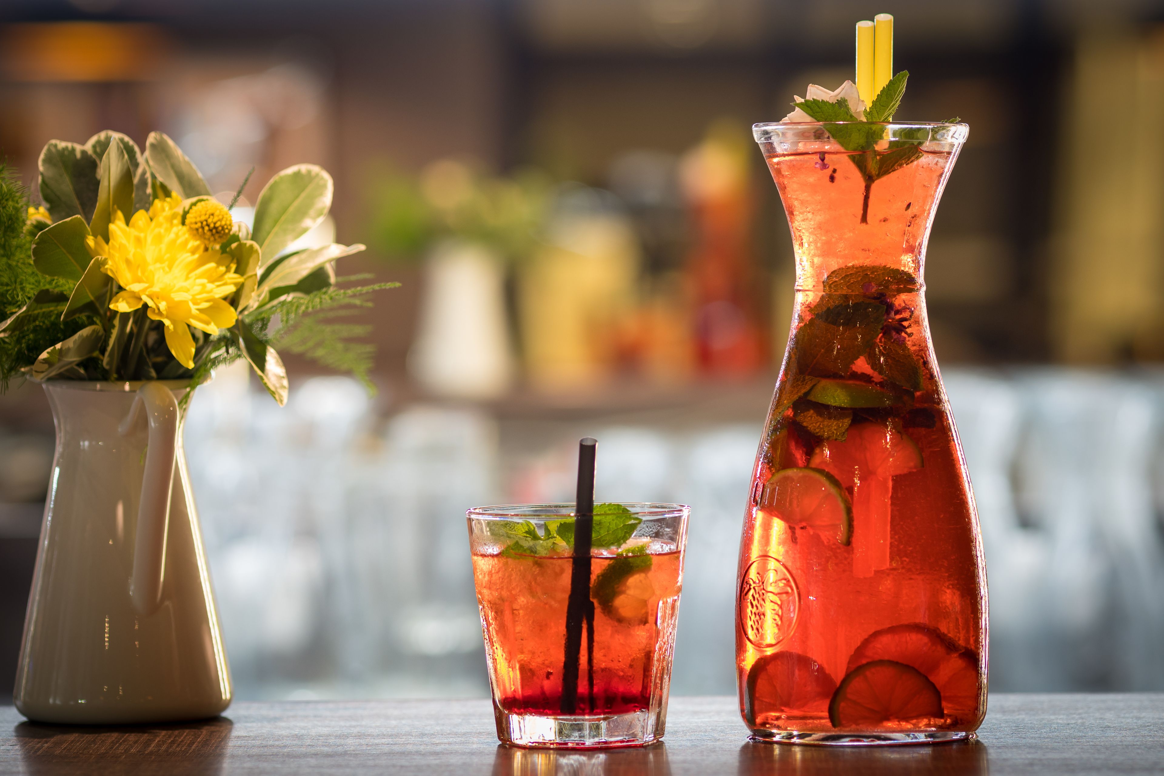 Un jarro y un vaso con una bebida, ambos con rodajas de lima y hojas de menta.