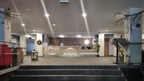 A hotel reception area with a modern design, including a reception desk, a staircase leading to the upper floor, and a decorative rug at the bottom of the stairs.