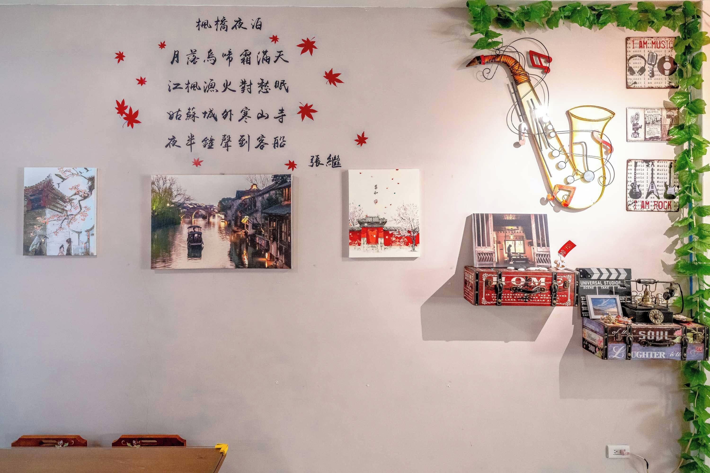 A wall with Chinese calligraphy, three framed paintings, and a saxophone sculpture.