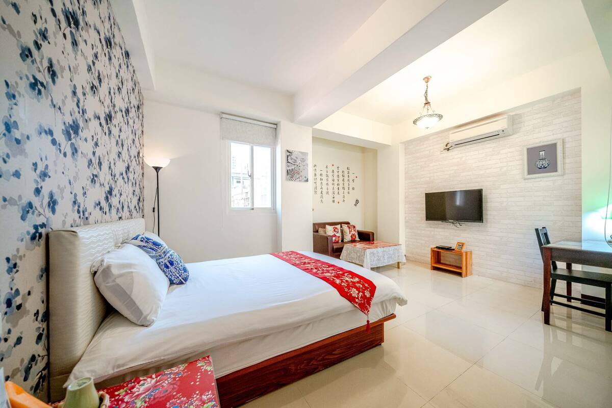 A modern bedroom with a large bed, a desk, a TV, and a dining table.
