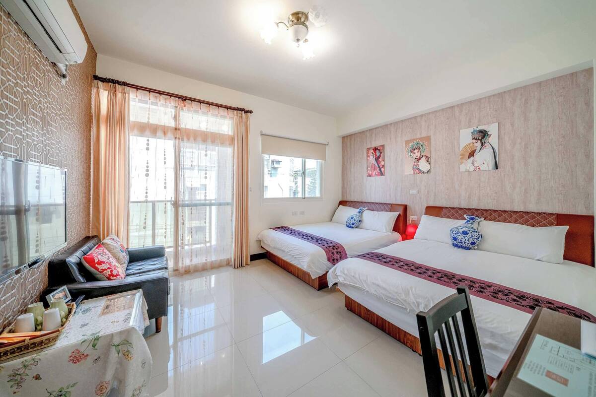 A hotel room with two beds, a sofa, a dining table, and artwork on the walls.