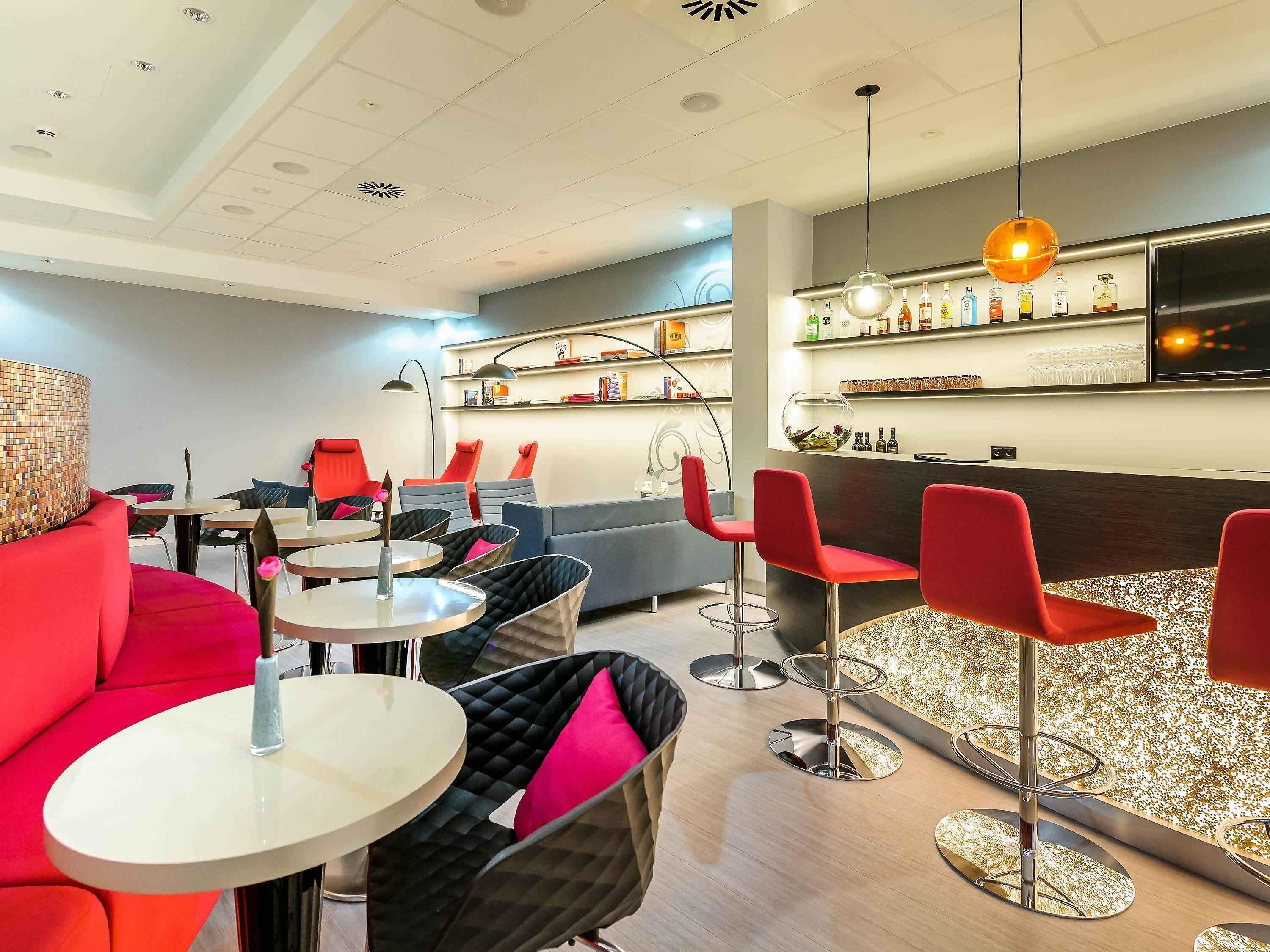 A modern bar area with round tables, red chairs, and a bar counter with shelves of bottles.