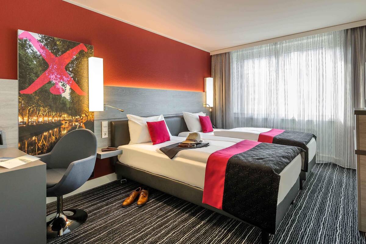 Quarto de hotel com duas camas, uma escrivaninha, uma cadeira, uma obra de arte grande e vista para um corpo d'água.