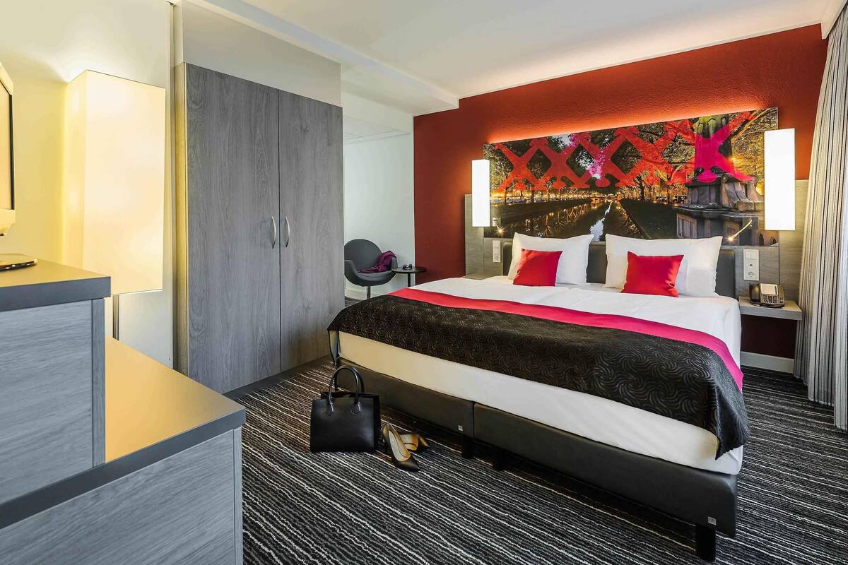 Ein Hotelzimmer mit Bett, Nachttisch, Lampe und Blick auf die Stadt.