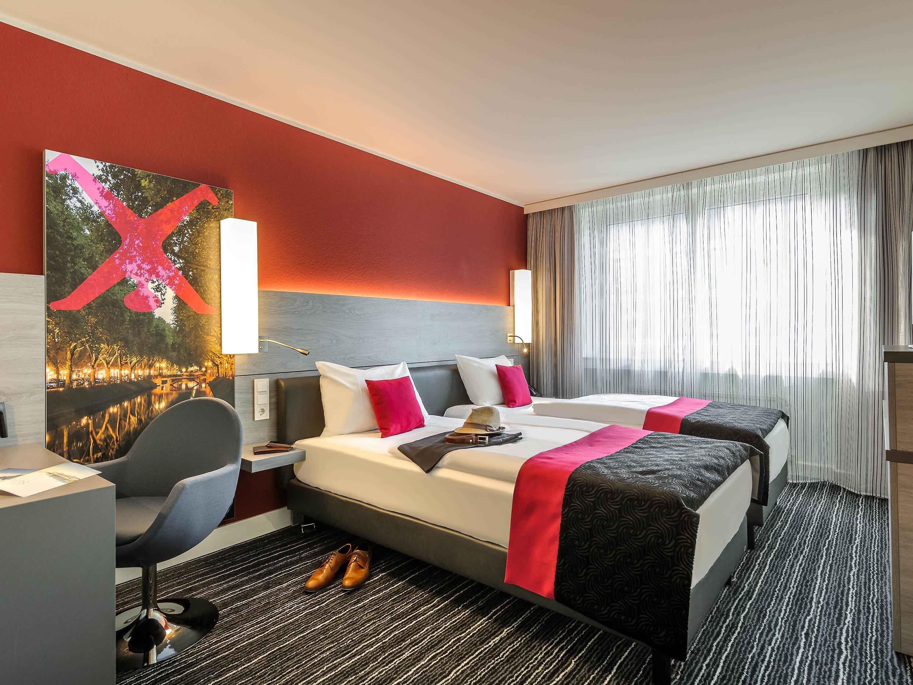 A hotel room with two beds, a desk, a chair, and a large painting on the wall.