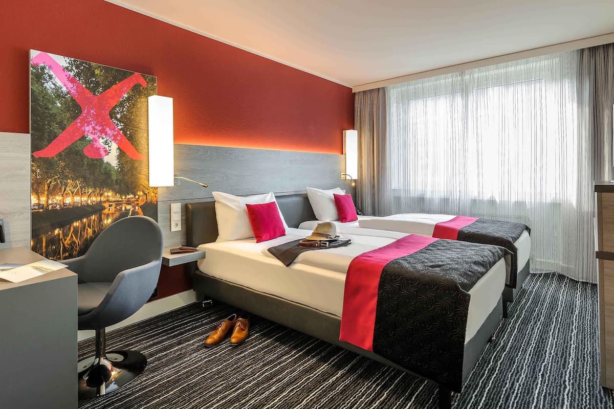 A hotel room with two beds, a desk, a chair, and a large painting on the wall.