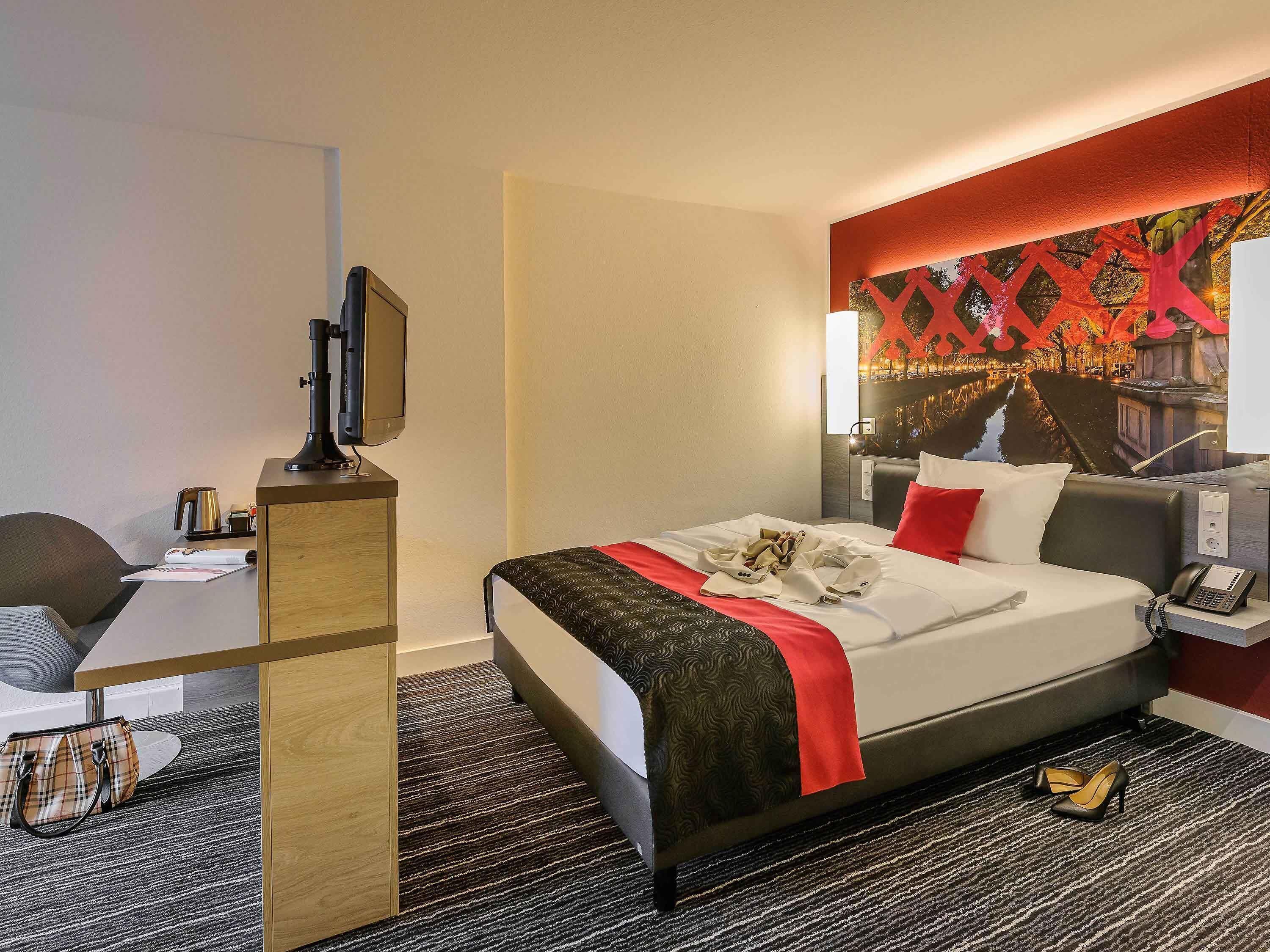 Habitación de hotel con cama, mesita de noche, escritorio, silla y una pared decorada con un mural.