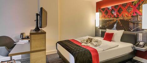 Habitación de hotel con cama, mesita de noche, escritorio, silla y una pared decorada con un mural.