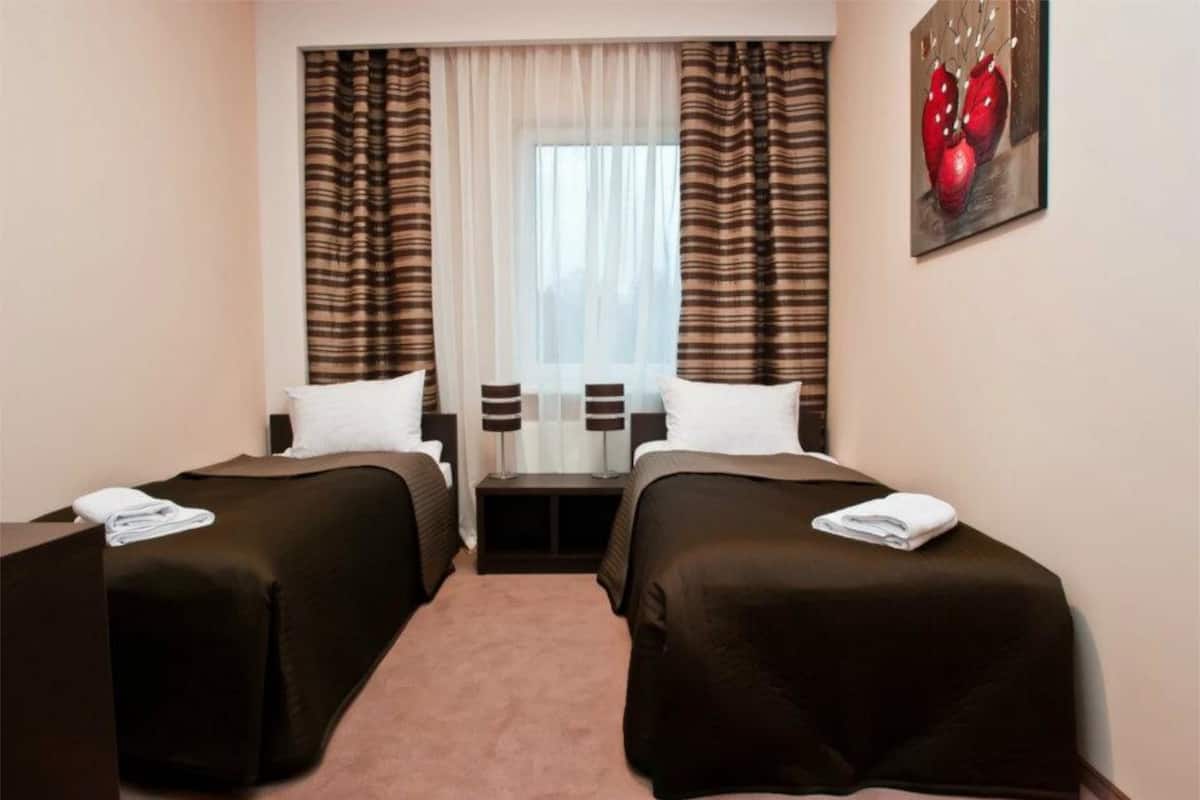 Una habitación de hotel con dos camas individuales, una mesita, una silla y un cuadro en la pared.