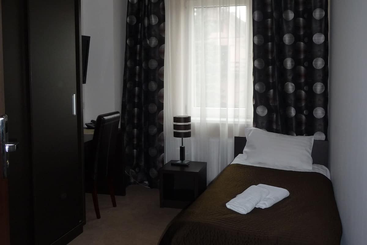 Habitación de hotel con cama, escritorio, silla, lámpara y armario.