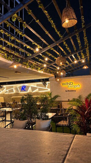 An outdoor seating area with tables and chairs, a pergola with hanging lights, and a sign for 'WIND Lounge by Residency.' - Residency Hotel Lekki Lagos (Lekki)