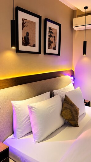 A hotel room with a bed, two framed artworks on the wall, a headboard with built-in lighting, and an air conditioning unit. - Residency Hotel Lekki Lagos (Lekki)