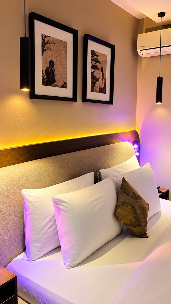 A hotel room with a bed, two framed artworks on the wall, a headboard with built-in lighting, and an air conditioning unit. - Residency Hotel Lekki Lagos (Lekki)