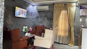 A hotel room with a marble wall, a flat-screen TV, a sofa, a table with a vase of flowers, and a curtain.