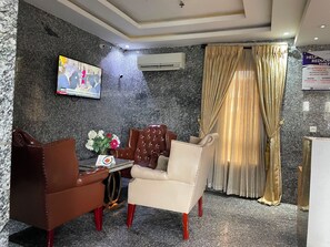 A hotel room with a marble wall, a flat-screen TV, a sofa, a table with a vase of flowers, and a curtain. - Residency Hotel Lekki Lagos (Lekki)